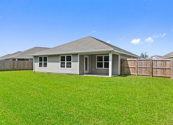 Backyard view of a single-story home with a covered patio and green lawn.