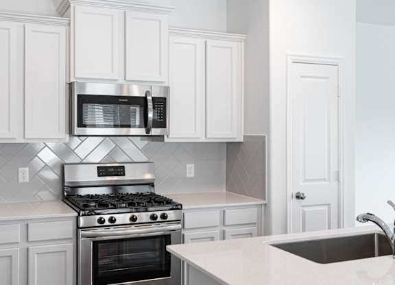 Houses in Humble, TX for Rent - Edgewater at the Lagoon - Kitchen with White Cabinets, Stainless Steel Appliances, Quartz Countertops, and Tile Backsplash