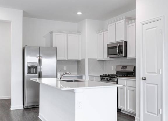 Apartments Humble, TX - Edgewater at the Lagoon - Kitchen with Vinyl Plank Flooring, White Quartz Countertops, White Cabinetry, Stainless Steel Appliances, Grey Herringbone Tile Backplash, and Cooking Island with a Sink.
