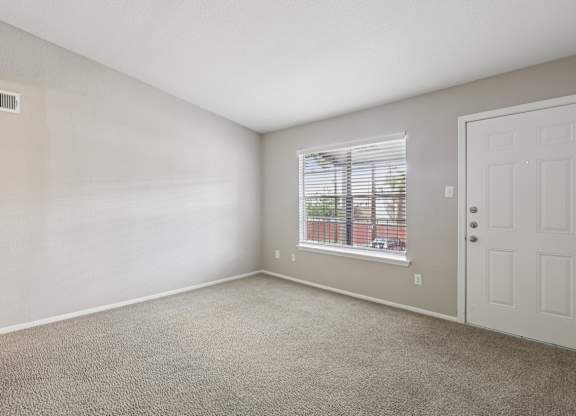 A room with a carpeted floor, a window with blinds, and a white door.