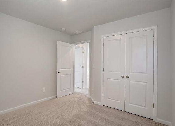 A room with white walls and carpeted floor with two white doors.