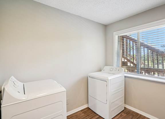 A white dryer and washer sitting next to a window in a laundry room.