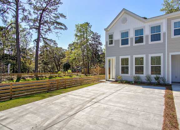 Pet-Friendly Homes for Rent in North Charleston, SC - Sumner Village - Front Exterior of Apartment Home with Driveway, Wooden Fence, and View of Trees and Bushes.