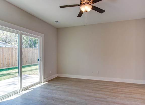 an empty living room with a sliding glass door and a ceiling fan