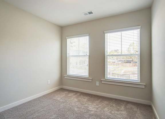 an empty room with two windows and a carpeted floor