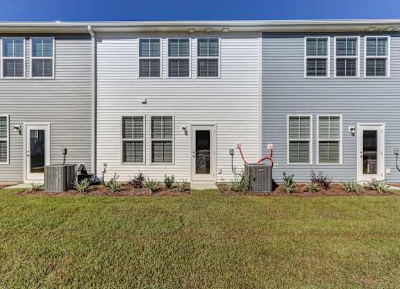 North Charleston, SC Townhomes Near The Citadel - Highland Townhomes - Exterior View of Townhomes with White and Grey Walls, and Backyards with Manicured Grass Lawns.