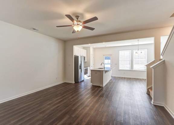 an empty living room with a ceiling fan and a kitchen