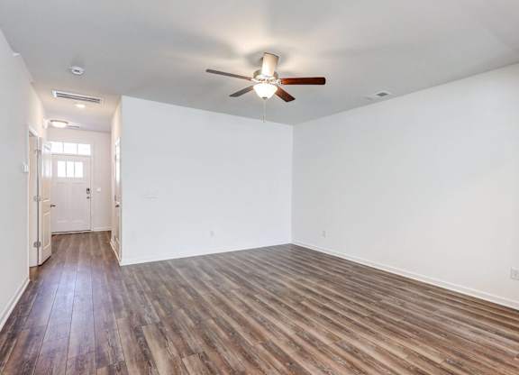 Four-BR Townhomes in North Charleston, SC - Highland Townhomes - Empty Living Room With White Walls, Wood-Style Flooring, and A Ceiling Fan