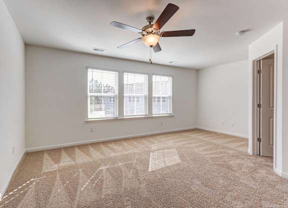 an empty living room with a ceiling fan and three windows
