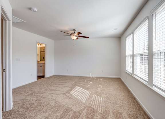an empty living room with large windows and a ceiling fan