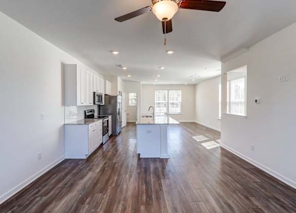 an empty living room with a ceiling fan and a kitchen