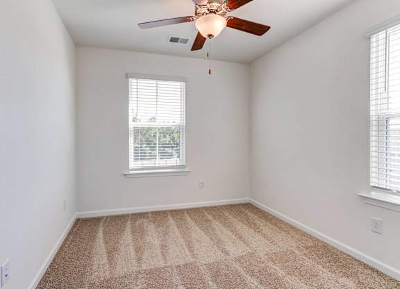 an empty room with a ceiling fan and two windows