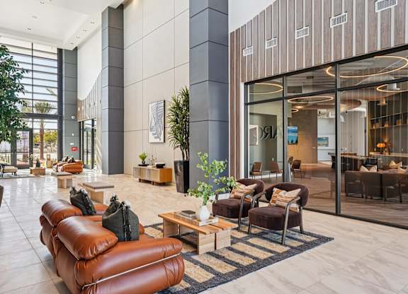 A modern living room with a brown leather sofa and a glass door leading to a balcony.