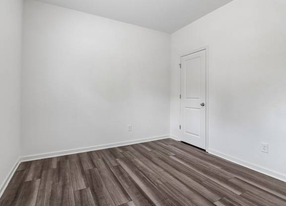 A room with a white door and wooden flooring.