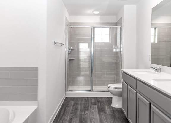 Dog-Friendly Homes for Rent in Humble, TX - Edgewater at the Lagoon - Bathroom with Hardwood Floor, Double Vanity Sink, Gray Cabinetry, Sliding Glass Door Shower, and Separate Bathtub.
