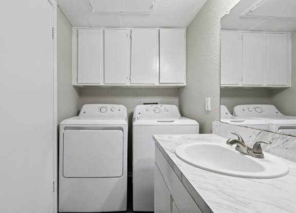 A white laundry room with a sink and cabinets.