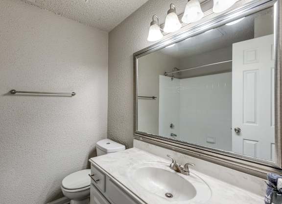 A bathroom with a toilet, sink, and mirror.