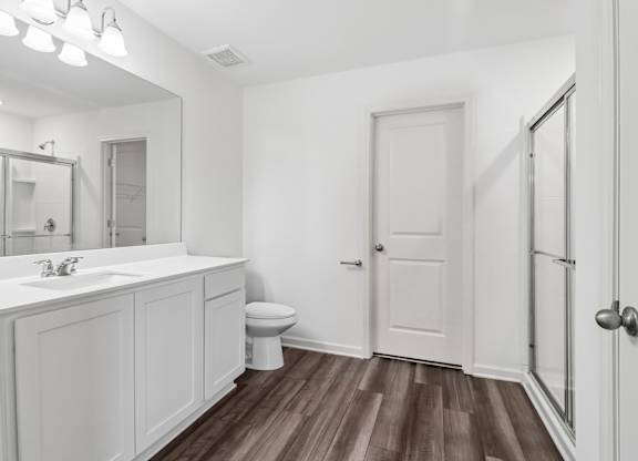 A white bathroom with wood flooring and a large mirror.