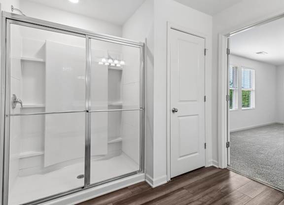 A white bathroom with a walk-in shower and a white door.