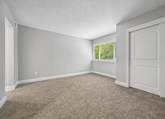 A room with a carpeted floor and a window with blinds.