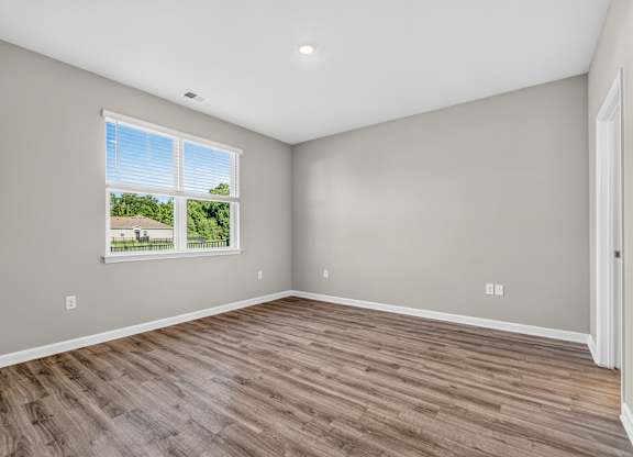 A room with wooden flooring and a window showing a view of a house and trees.
