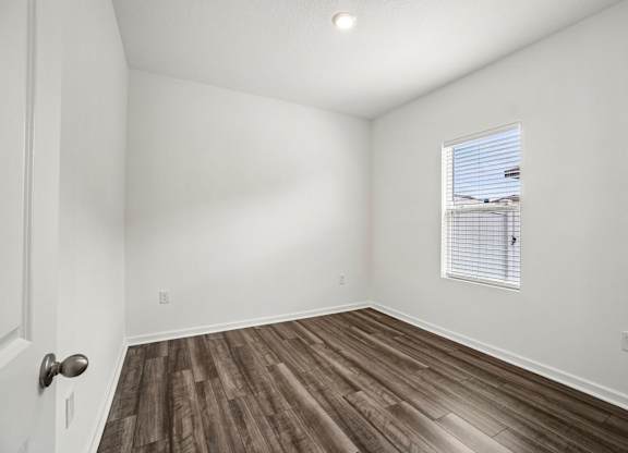 A room with wooden flooring and a window with blinds.