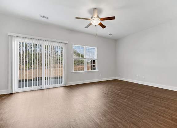 Cottonvale Towns in Savannah, GA photo of living room with large windows, ceiling fan, and hardwood flooring