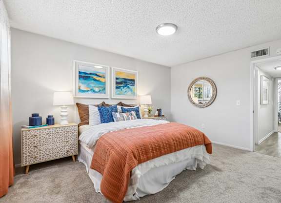 A bedroom with a bed, nightstand, and two paintings on the wall.
