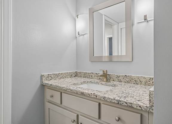 A bathroom with a marble countertop and a mirror above it.