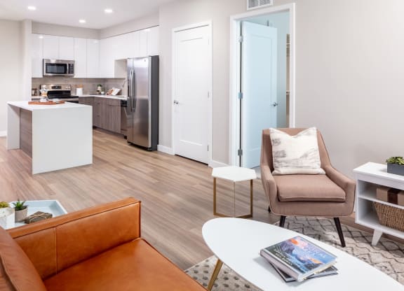 a living area with a couch chair coffee table and a kitchen in the background