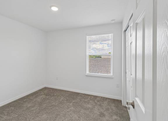 A room with a carpeted floor and a window with blinds.