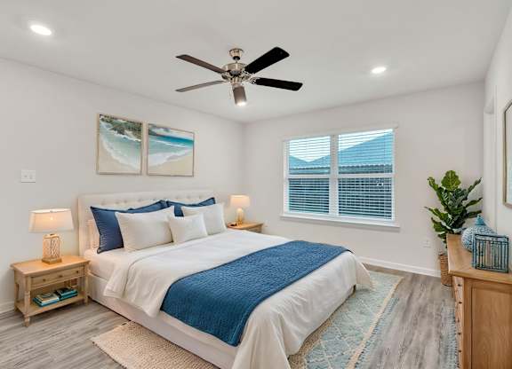 A bedroom with a bed, a ceiling fan, and a painting on the wall.