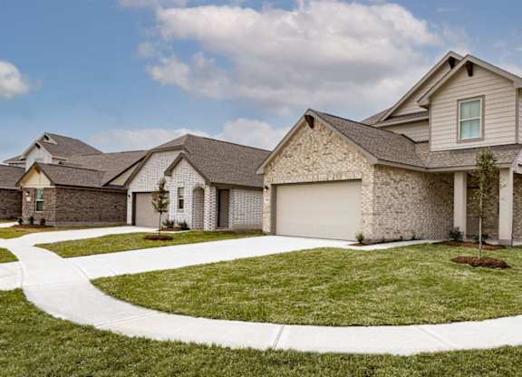 Apartments for Rent in Humble, TX - Edgewater at the Lagoon - Exterior of Homes with Attached Garages, Grass Lawns, and Concrete Walkway.