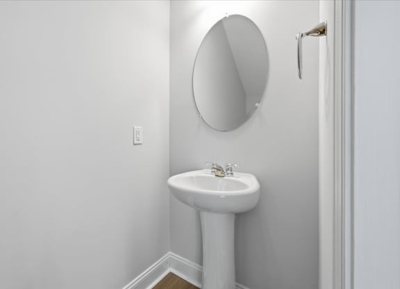 A white pedestal sink with a round mirror above it.
