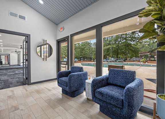 Two blue chairs are placed in a room with a view of a pool and trees outside.
