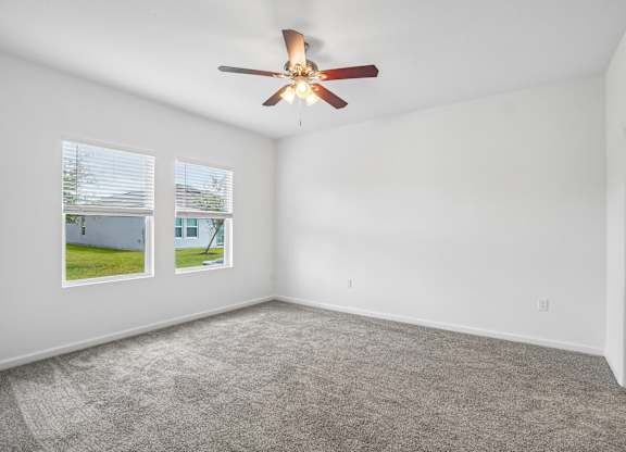 A room with a ceiling fan and two windows.