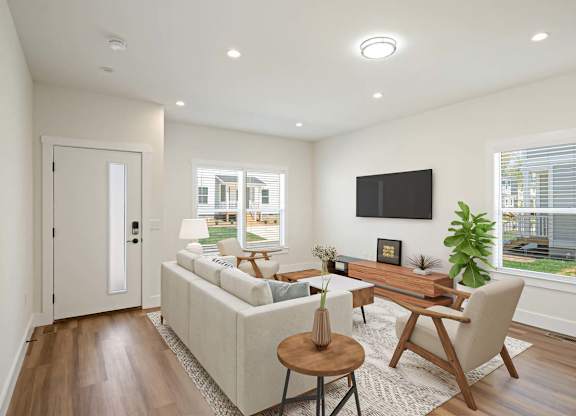 A modern living room with a white sofa, a wooden coffee table, and a flat-screen TV mounted on the wall.