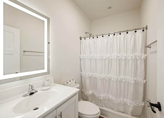 Modern bathroom with white vanity, lighted mirror, and shower curtain in a clean, minimalist design.