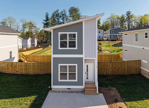 A small house with a grey and white exterior is surrounded by a wooden fence.