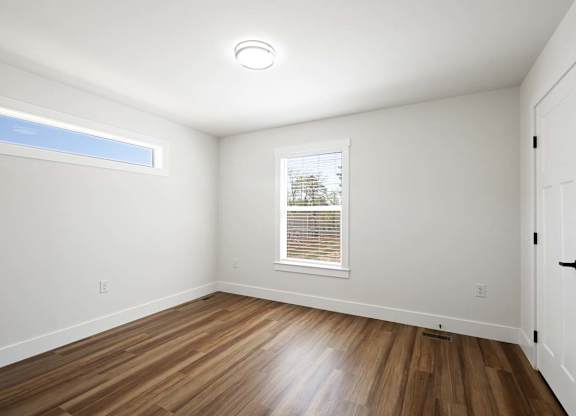 Bright bedroom with natural light, white walls, and wood-style flooring in a modern house.