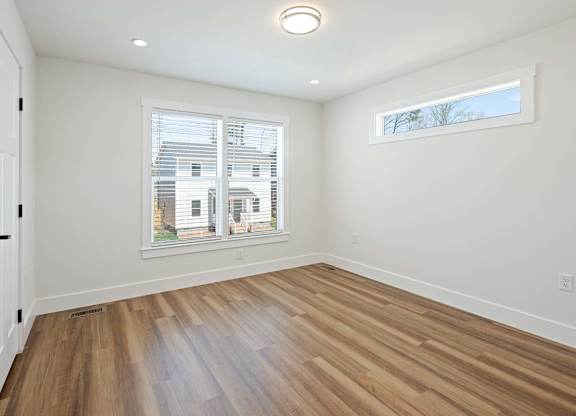 A room with wooden flooring and a window showing a view of a building outside.