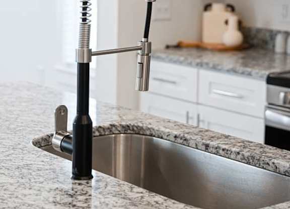Close-up of a modern kitchen faucet with a pull-down sprayer and granite countertop.