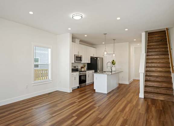 Open-concept home kitchen with stainless steel appliances, white cabinetry, and wide plank wood flooring.