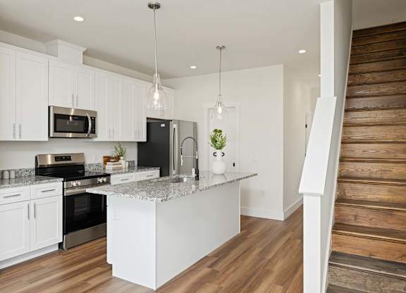 Modern kitchen with white cabinets, center island, stainless steel appliances, and pendant lighting.