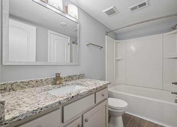 A bathroom with a marble countertop and white fixtures.