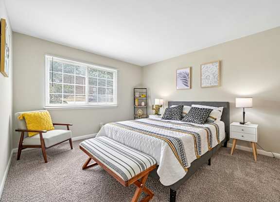 A bedroom with a bed, nightstand, chair, and window.