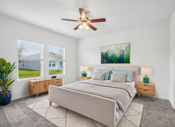 A bedroom with a large bed, a ceiling fan, and a painting on the wall.