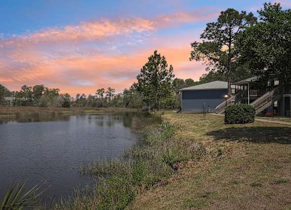 A serene landscape with a house and a pond at sunset.