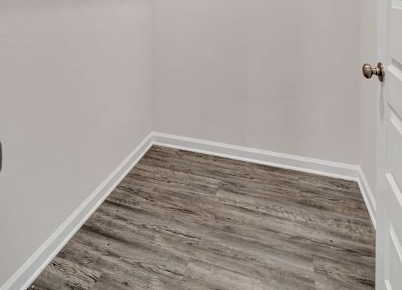 A walk-in closet with a wooden floor and white walls.
