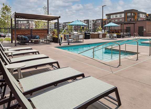A pool area with sun loungers and a building in the background.